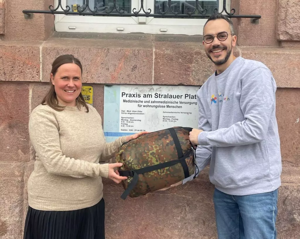 Fayez und ein Freiwilliger von „Schenk doch mal ein Lächeln“ halten einen Schlafsack vor der Praxis am Stralauer Platz.